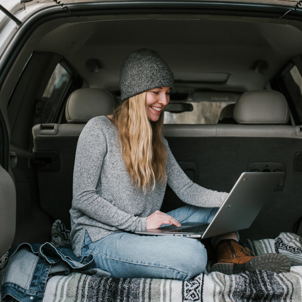 Girl in a wool hat with a laptop writing a blog in her car